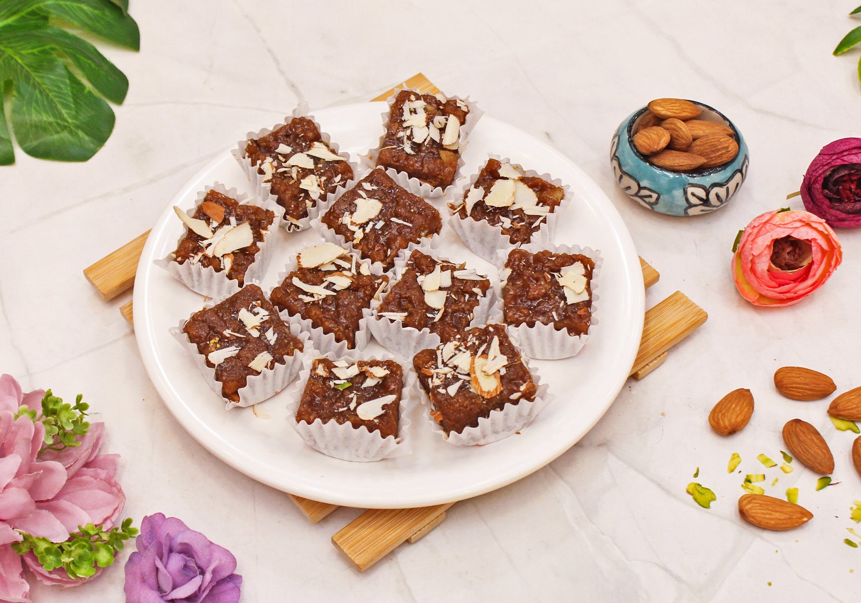 Sairam Special Dhodha with almonds and nuts on a white plate, surrounded by flowers and nuts on a light surface.