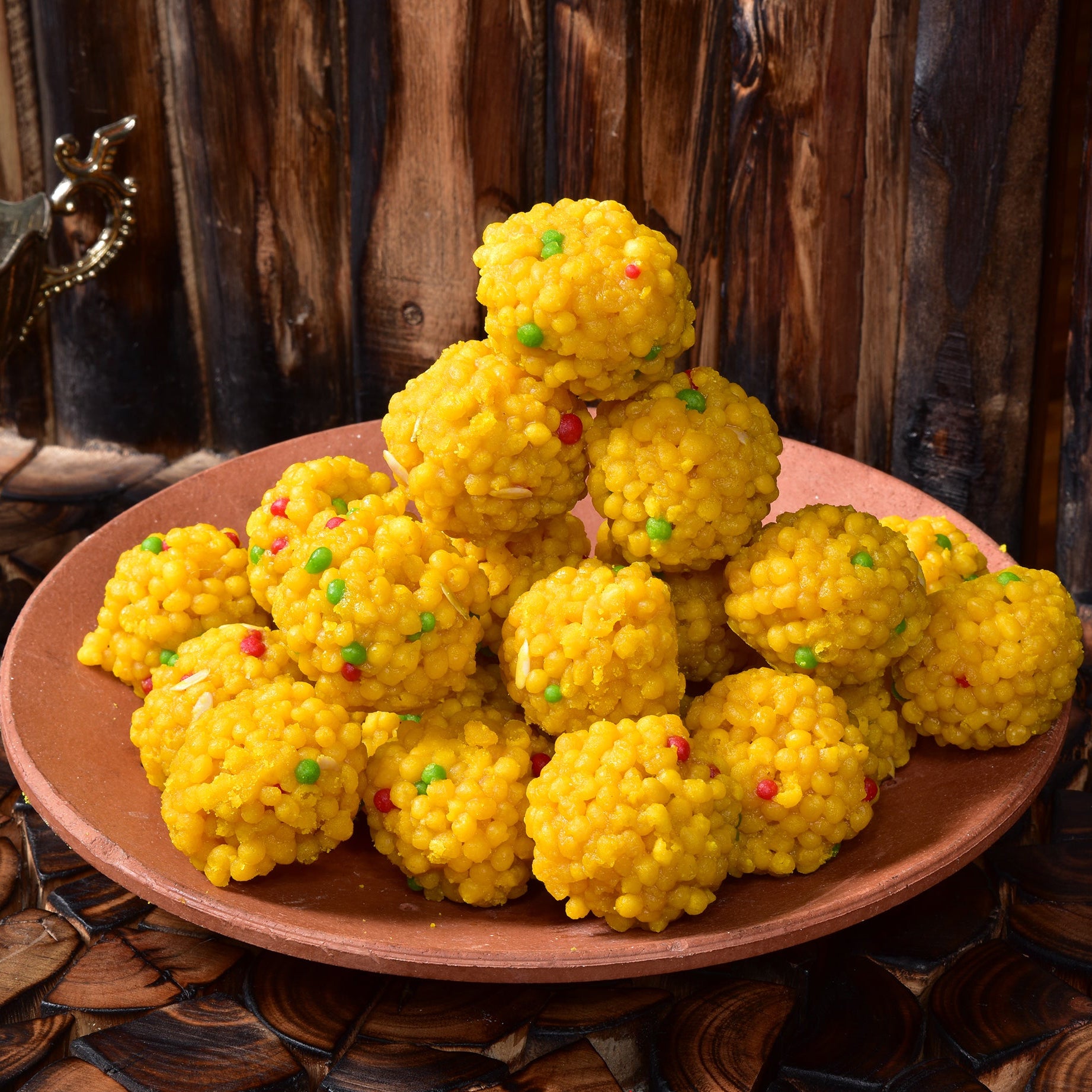 Yellow spherical sweets with colorful sprinkles on a wooden plate against a rustic background.